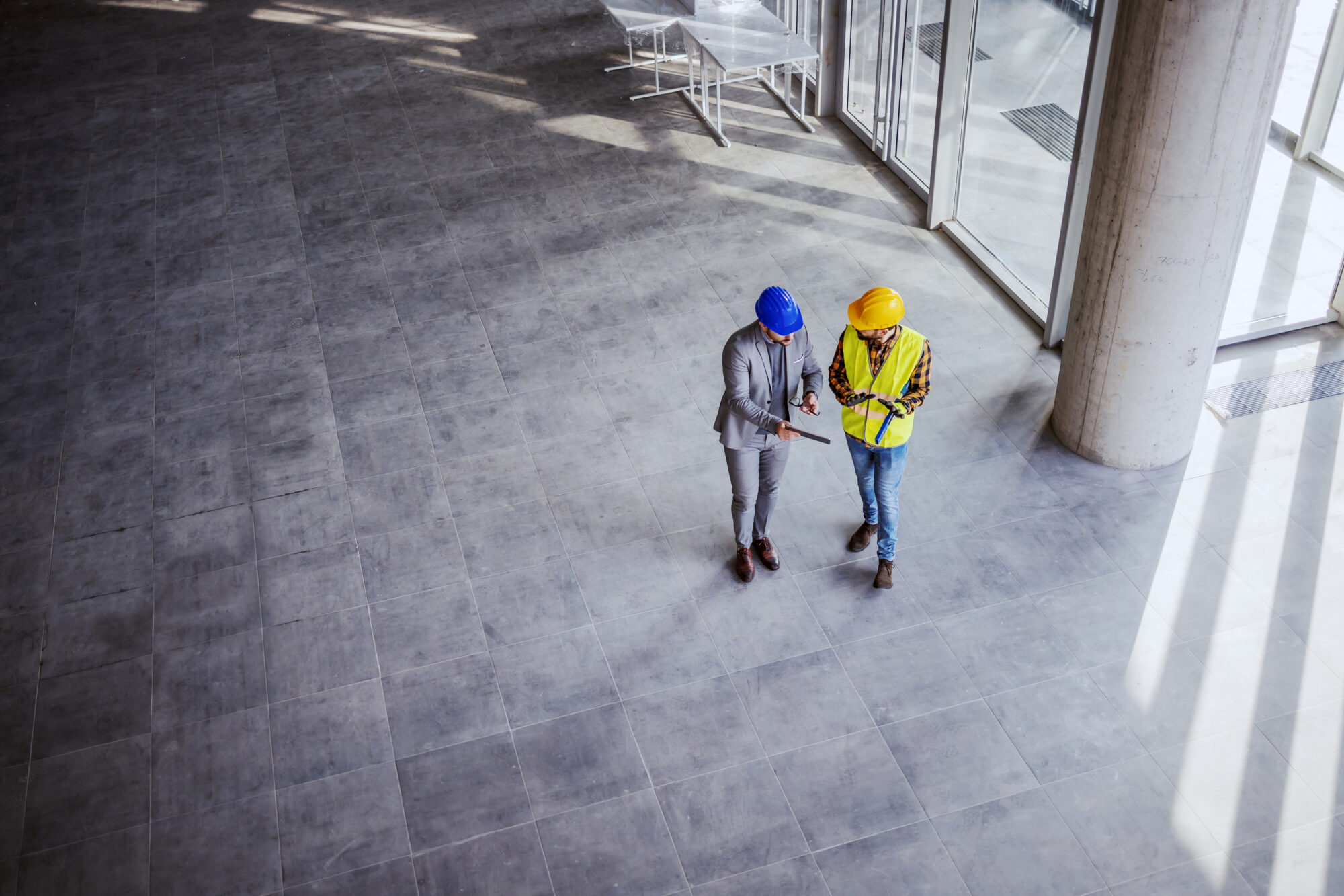 Top view of architect holding tablet and talking with construction worker about new ideas on project they working on. Building in construction process interior.